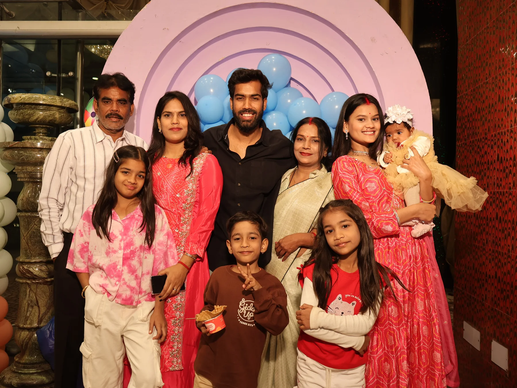 A group of adults and children posing in front of a birthday balloon backdrop