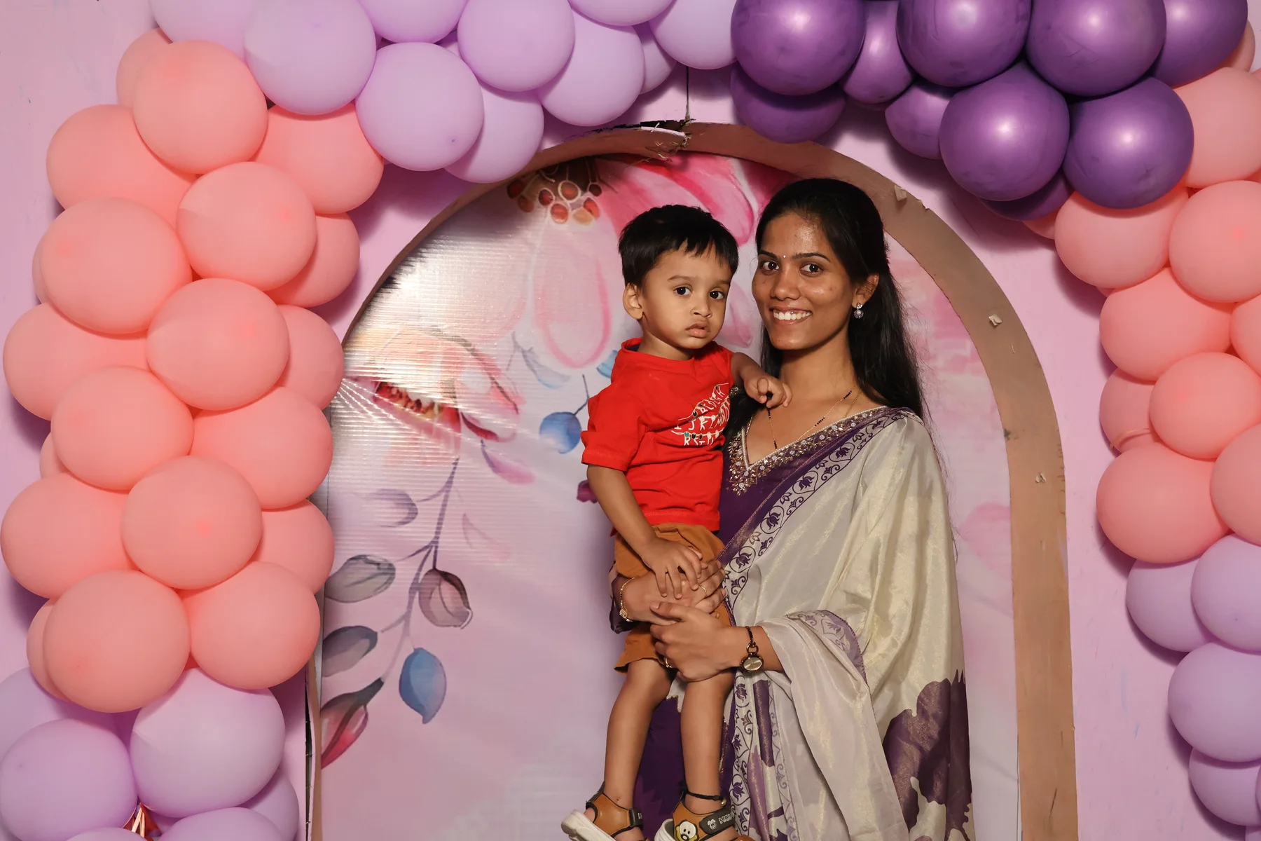 A guest holding a child in front of a pastel balloon celebration backdrop